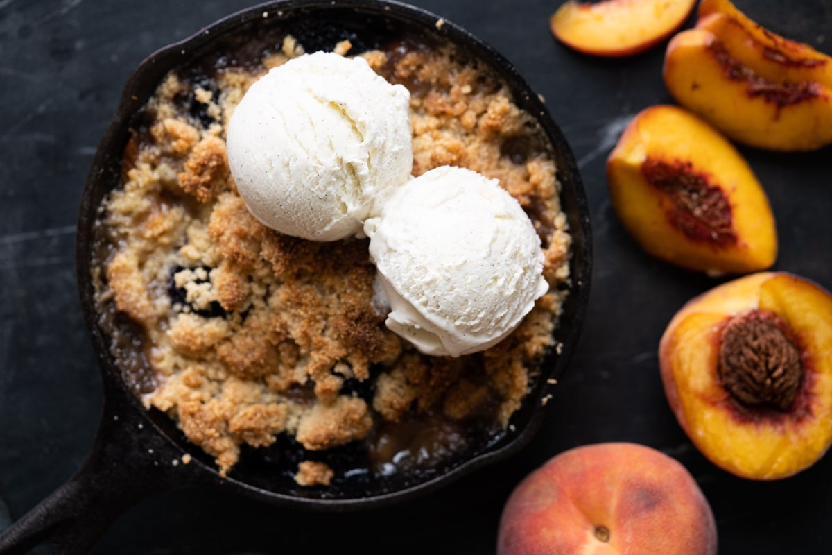 Freshly baked peach and blackberry crisp with two scoops of vanilla ice cream