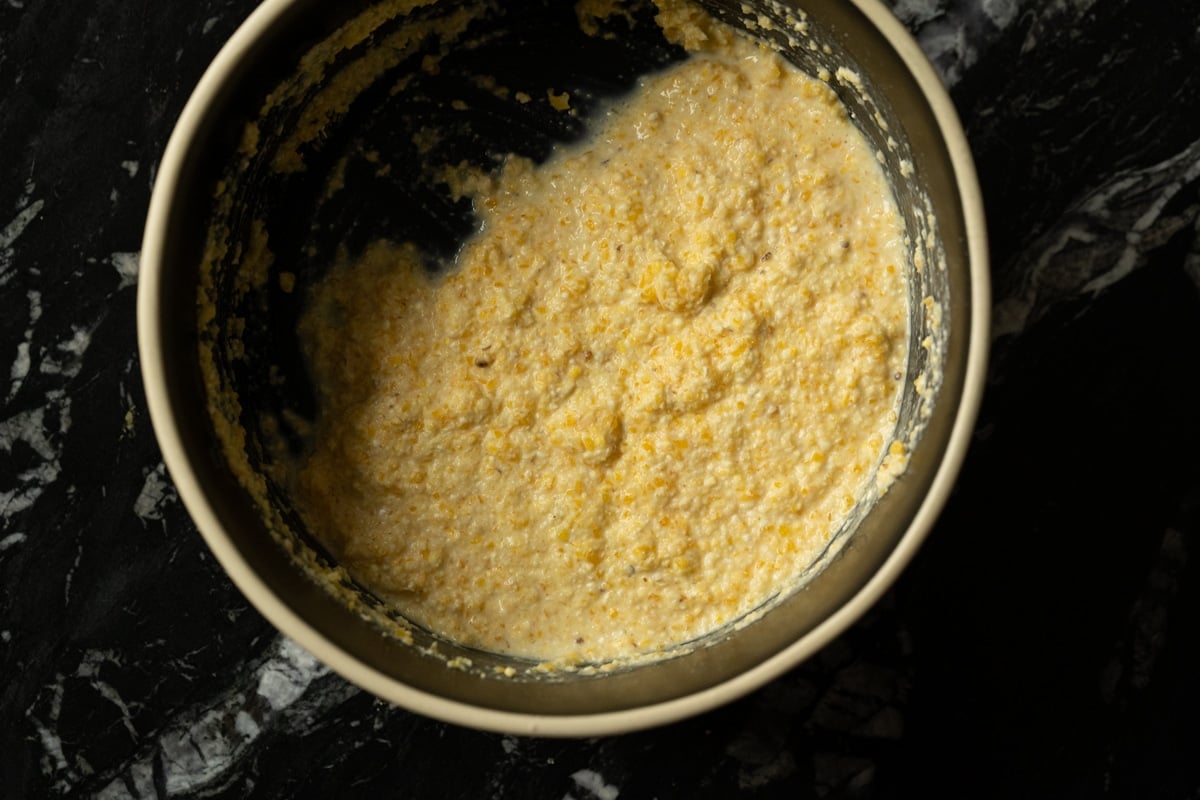 Medium grind cornmeal soaking with buttermilk in a black bowl