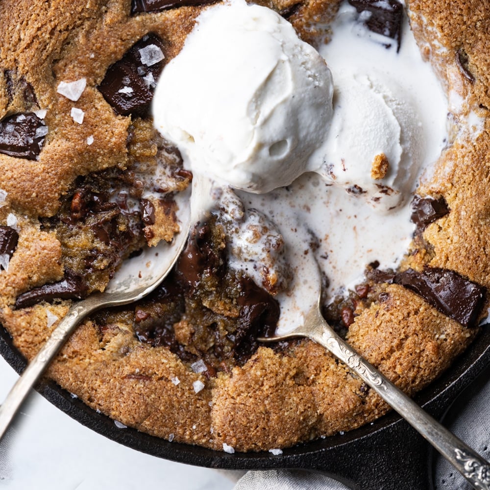 Two spoons eating gooey chocolate keto skillet cookie with melting vanilla ice cream
