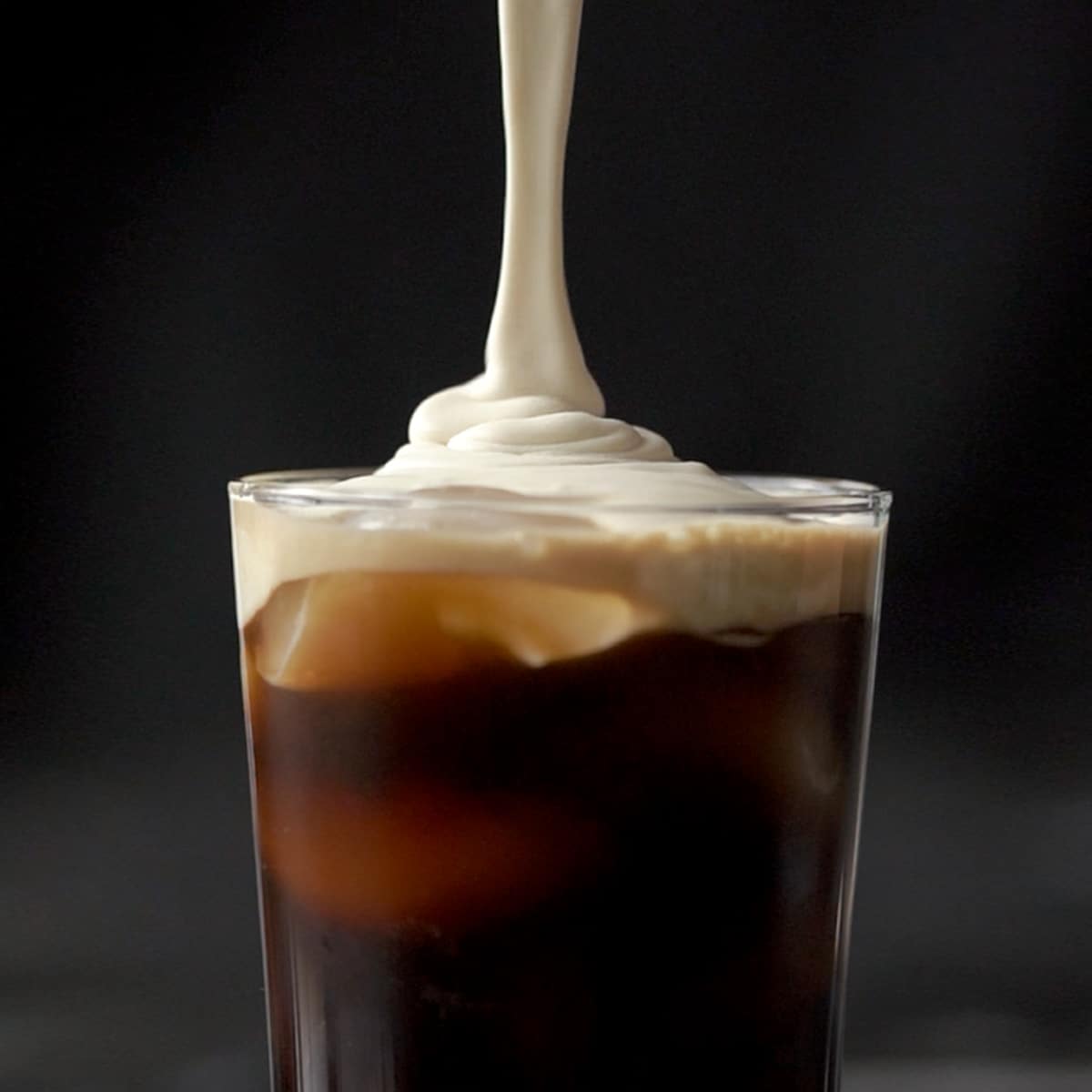 Pouring the salted caramel cream onto a tall glass with cold brew and ice