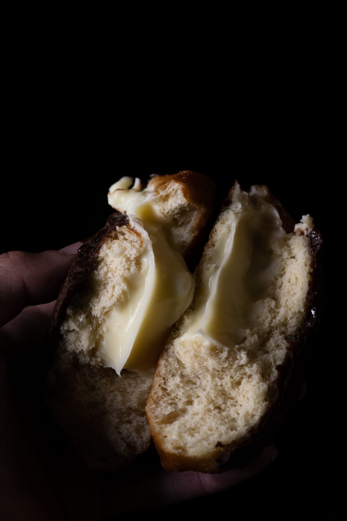 Holding a halved keto boston cream donut showing the creamy vanilla custard filling and fluffy texture
