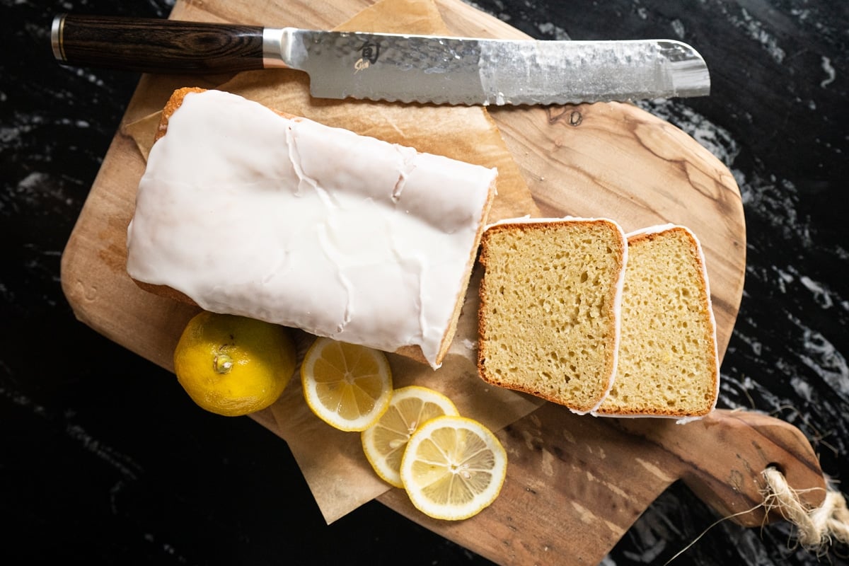 Slicing a loaf of keto lemon pound cake with a serrated knife