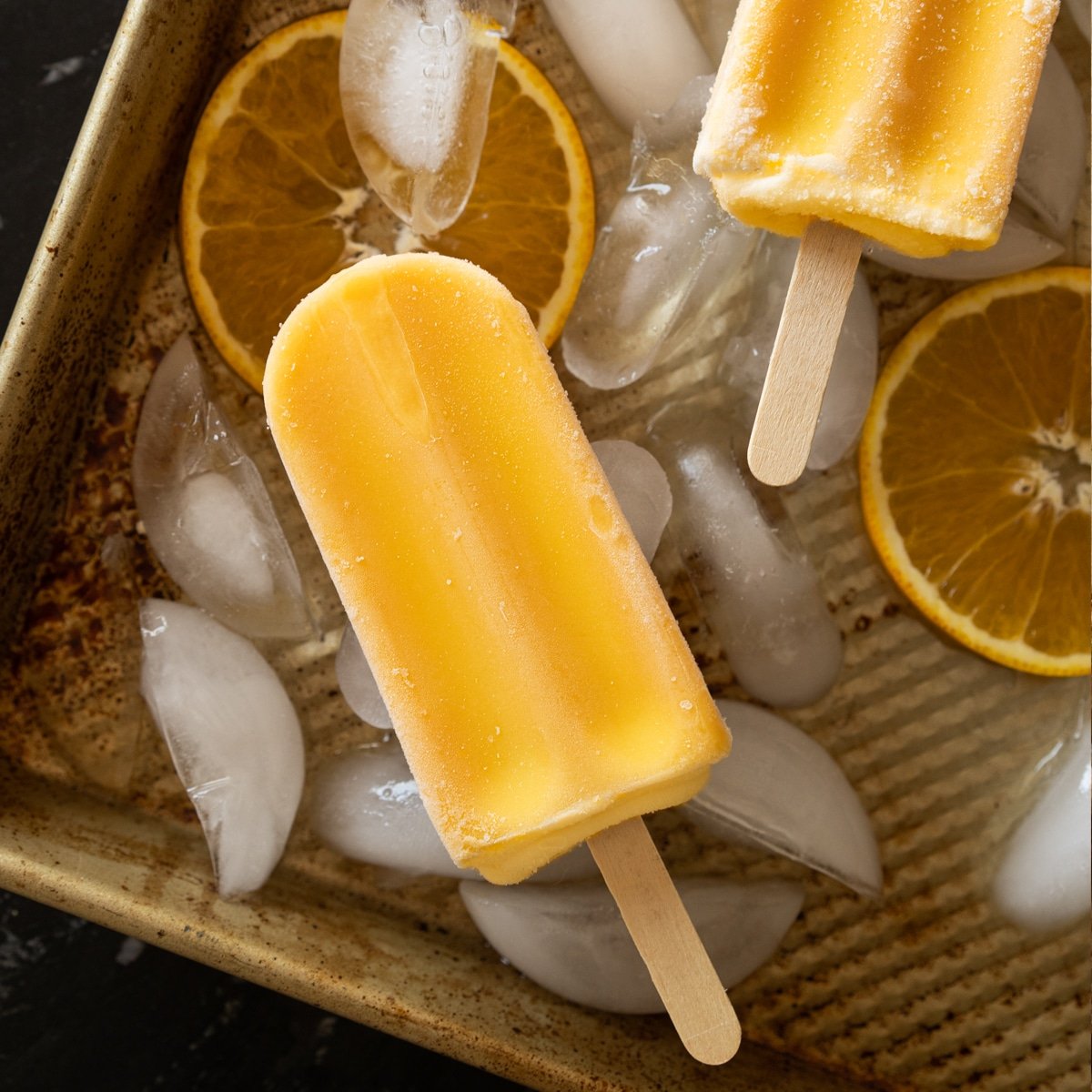 Keto orange creamsicle popsicles on a baking tray with ice