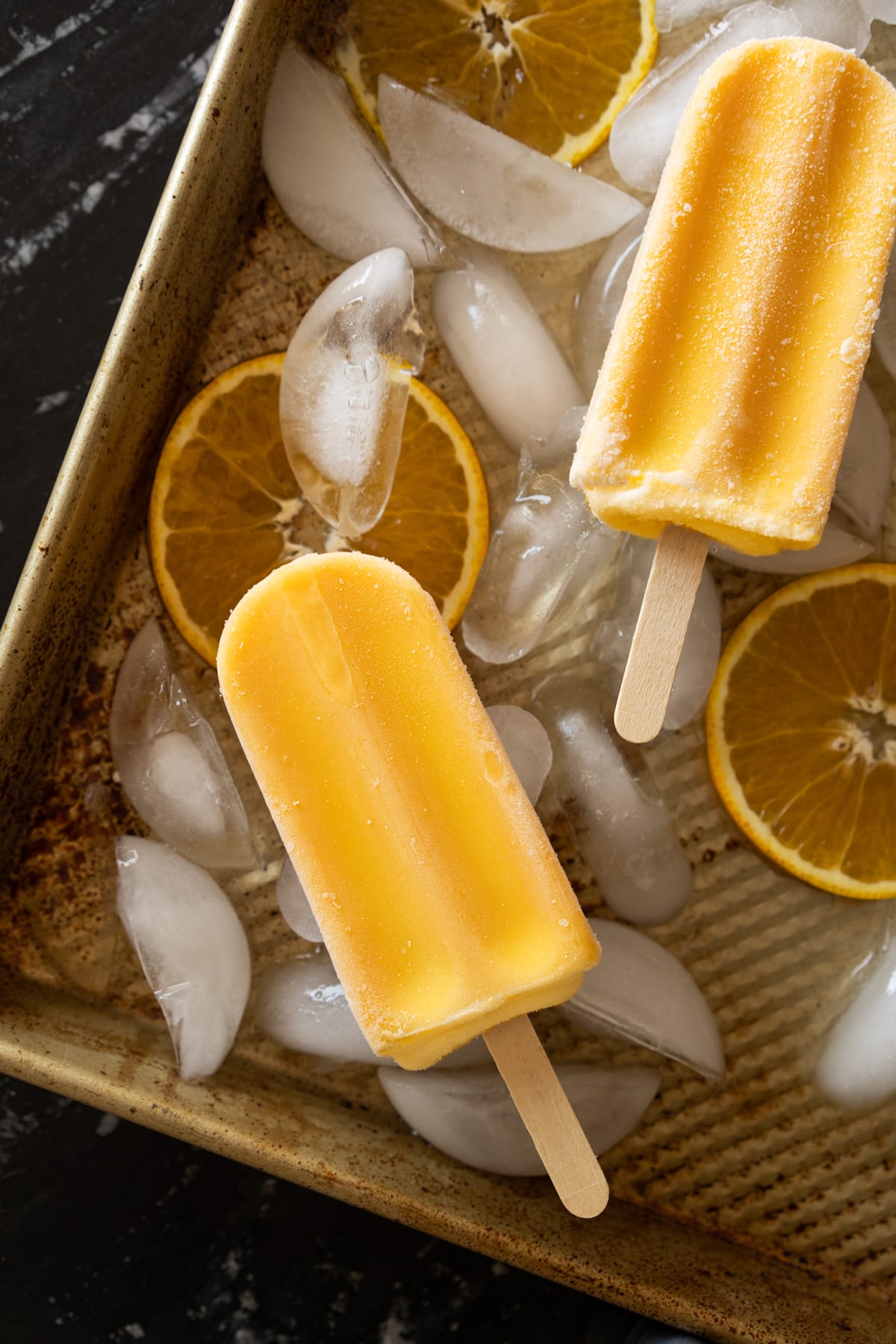 Keto orange creamsicle popsicles on a baking tray with ice