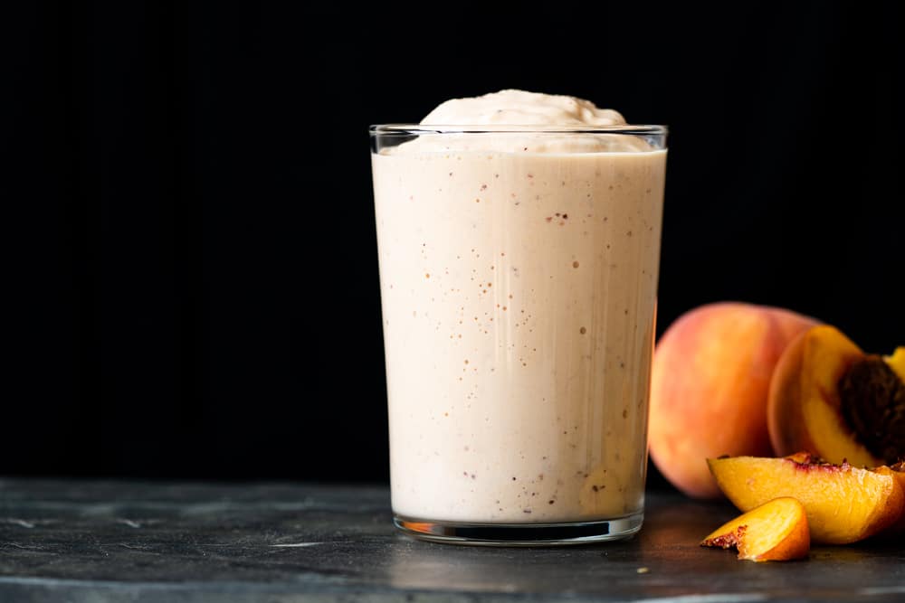 Side shot of a keto peach milkshake in a glass showing its thick texture