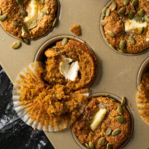 Keto pumpkin cream cheese muffins on a baking tray with pumpkin seeds