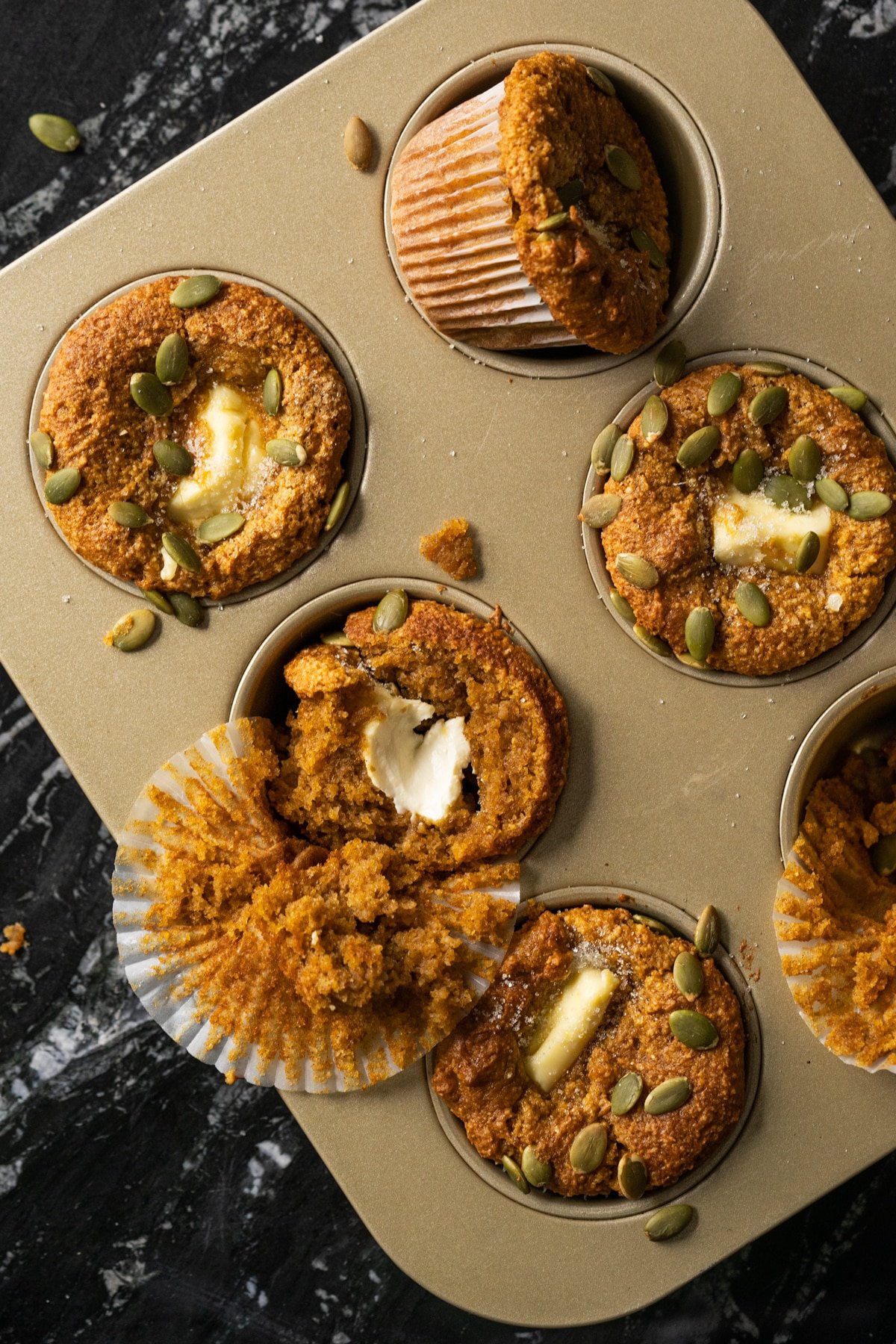 Keto pumpkin cream cheese muffins on a baking tray with pumpkin seeds