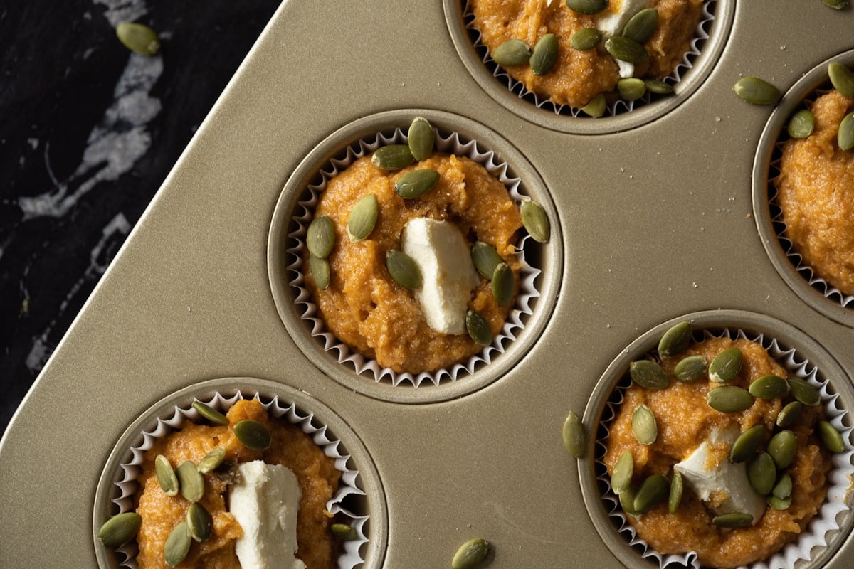 Unbaked keto pumpkin cream cheese muffins on a tray with paper liners