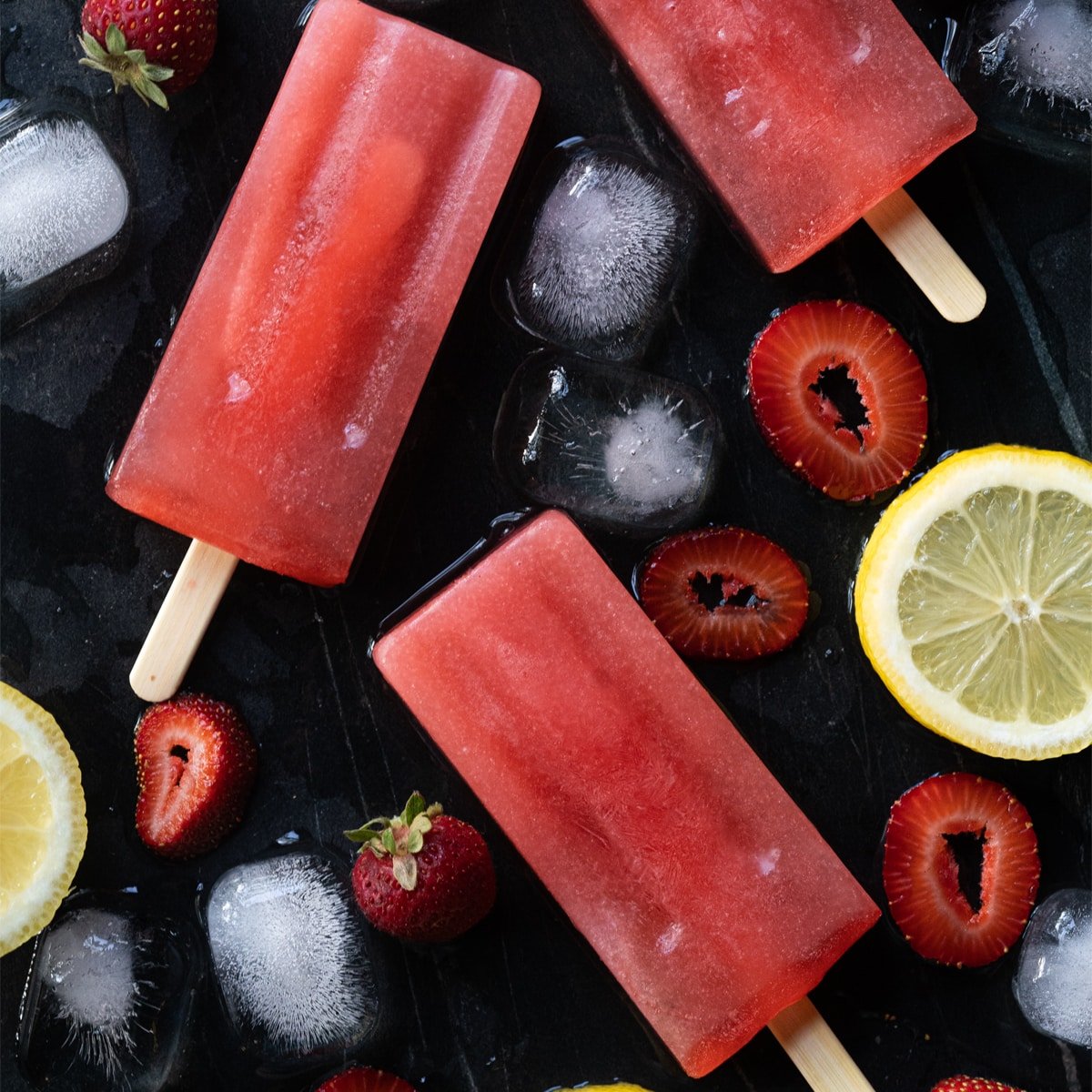 Keto strawberry lemonade popsicles on black marble with ice
