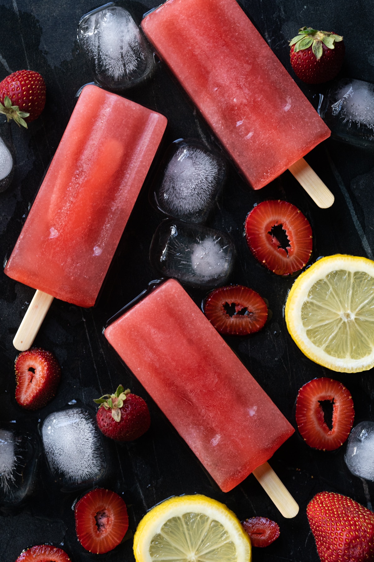Keto strawberry lemonade popsicles on black marble with ice