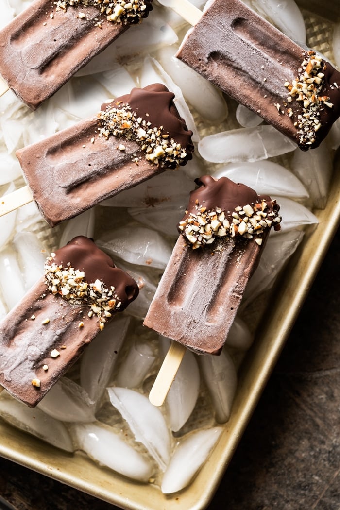 Keto chocolate popsicles on a golden baking tray with ice