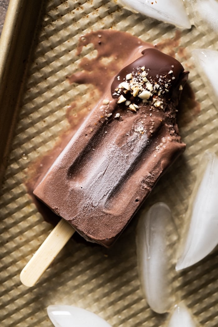 Bitten and melting paleo chocolate popsicle on a golden baking tray
