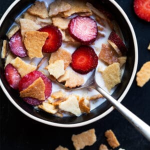 Keto Frosted Flakes cereal with sliced strawberries and almond milk in a black bowl