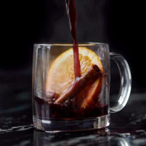 Pouring a refined sugar free keto mulled wine onto a glass mug with an orange slice and cinnamon stick