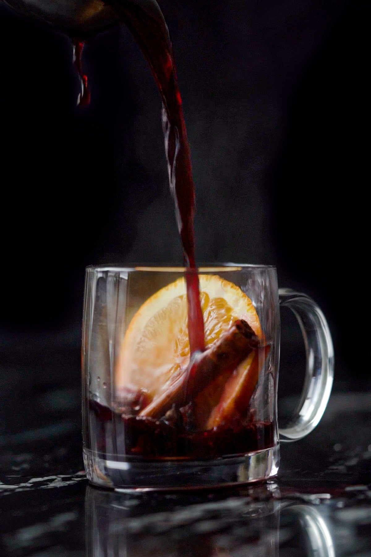 Pouring a refined sugar free keto mulled wine onto a glass mug with an orange slice and cinnamon stick 