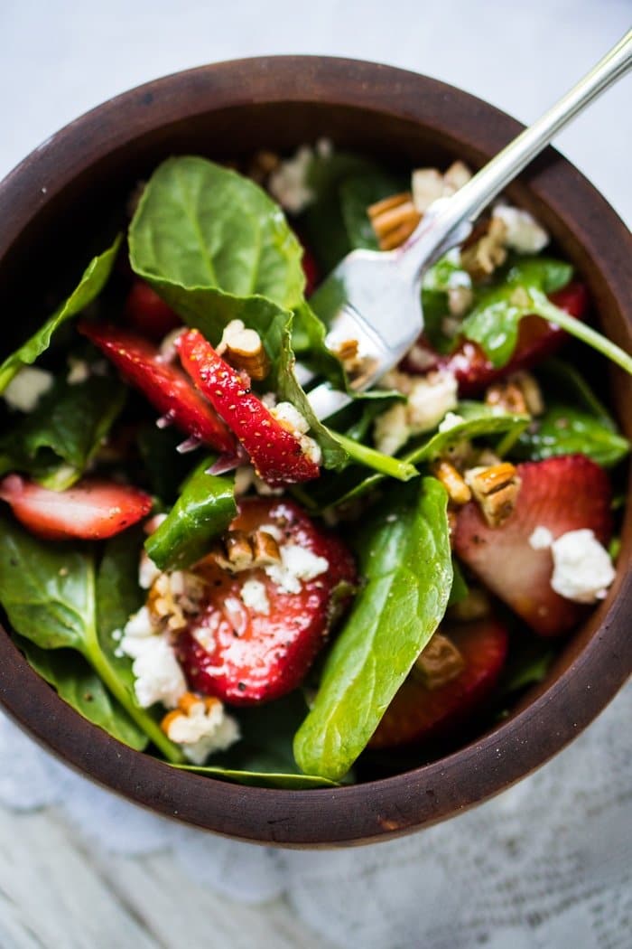 Eating strawberry spinach salad with a fork in a wooden bowl