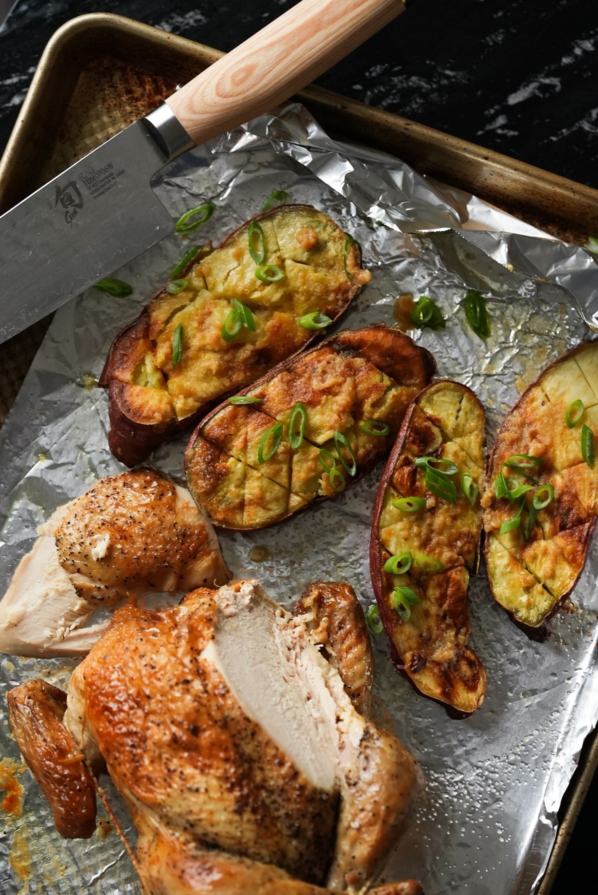 Roasted Japanese sweet potatoes with miso butter and fresh scallions and a roast chicken on a baking tray