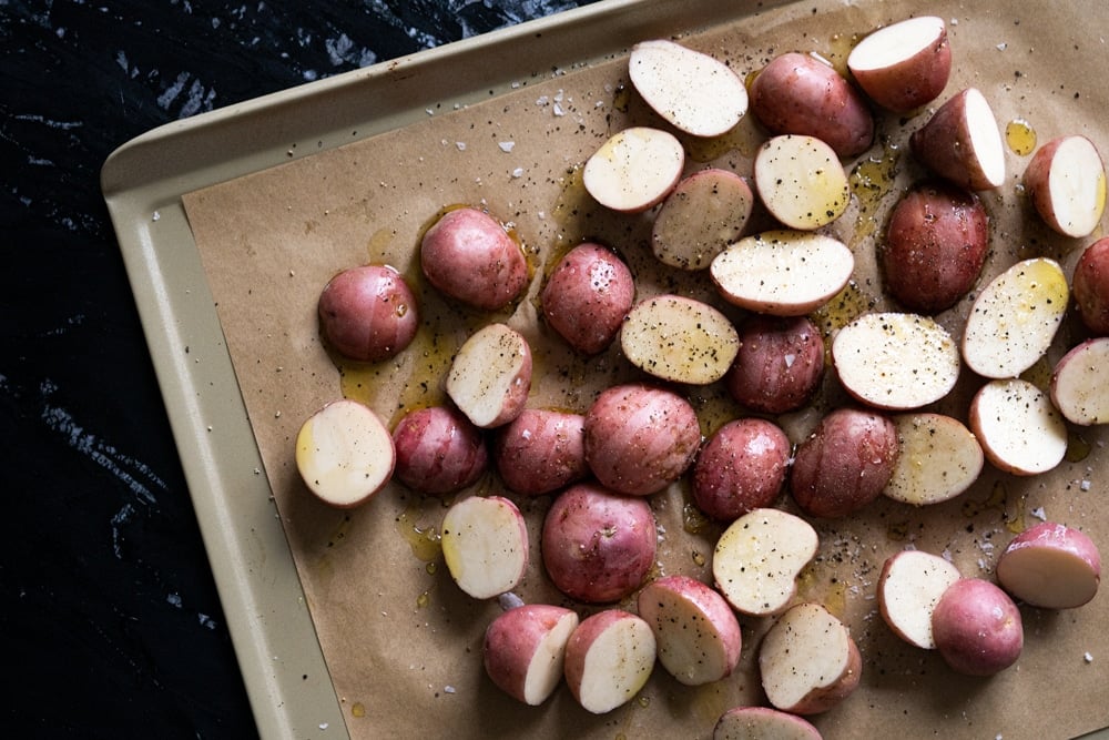 Halved raw potatoes on a baking tray with parchment paper