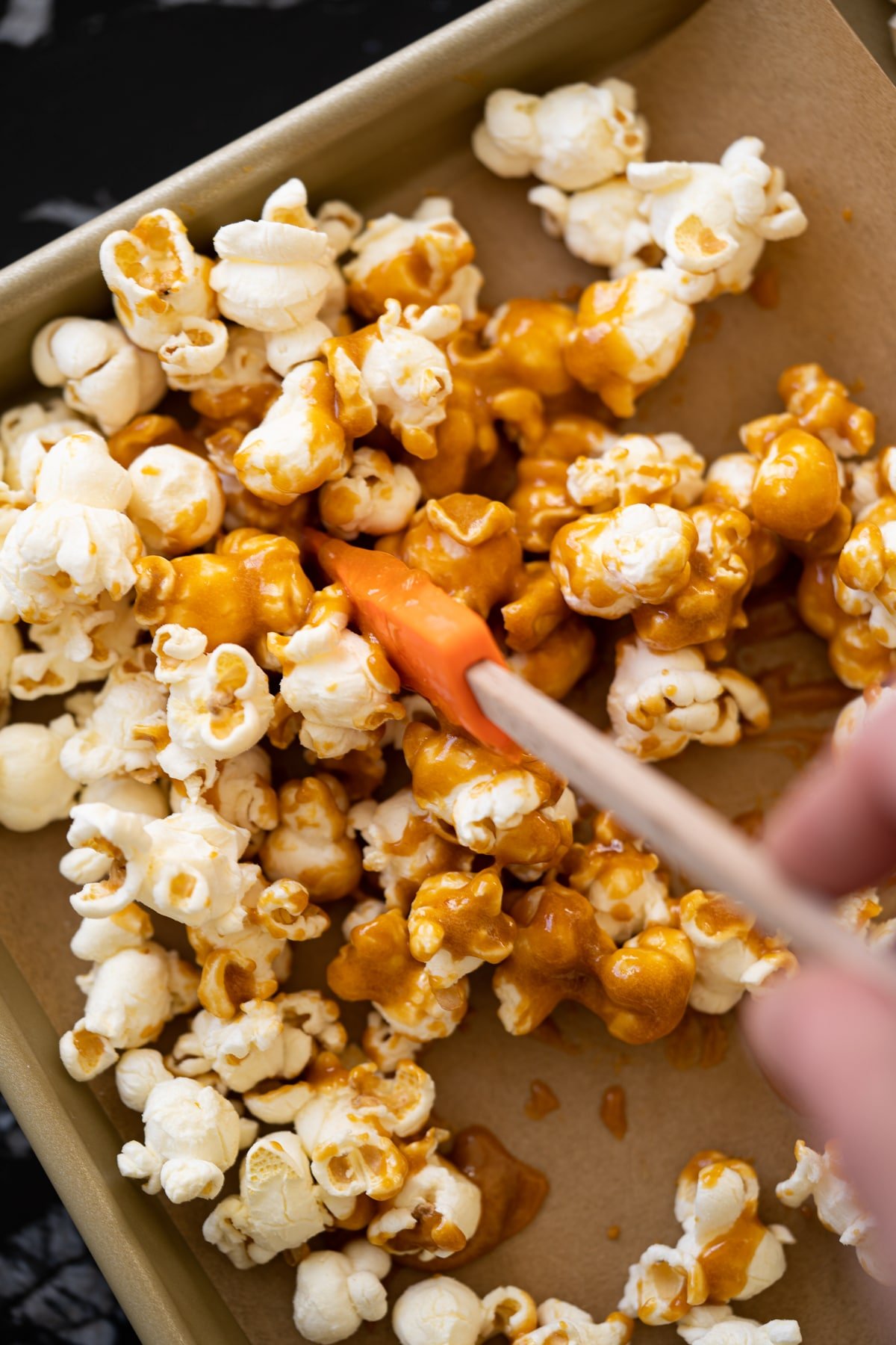 Mixing popcorn with keto caramel on a lined baking tray